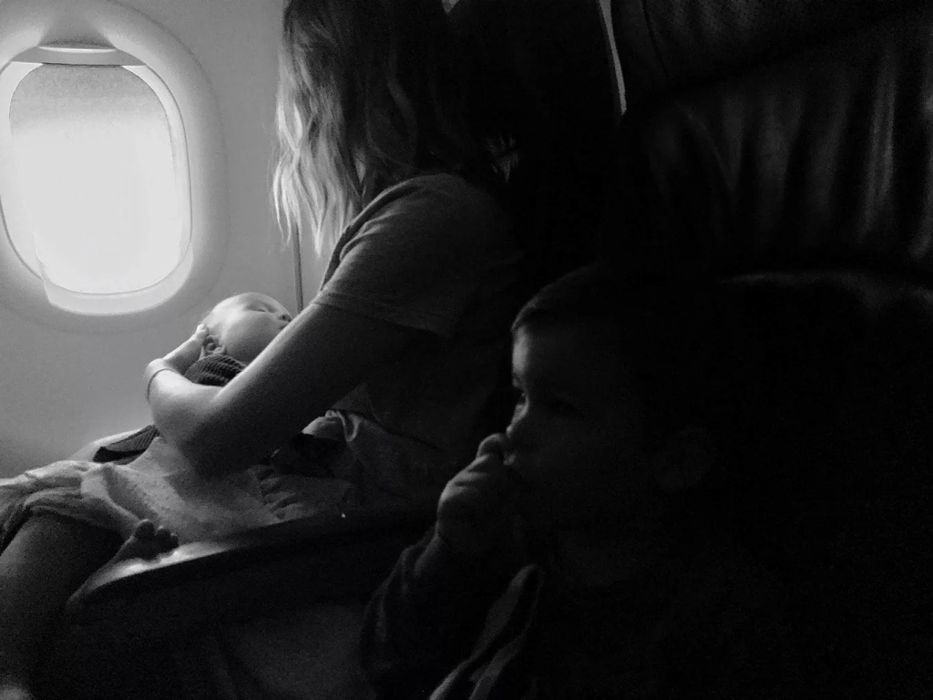 مادری که کودکش رو در هواپیما در آغوش گرفته است و کنارش کودک دیگرش نشسته است