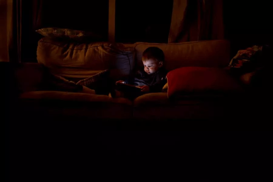 یک کودک در اتاقی تاریک که نور تبلت روی صورت آن افتاده است